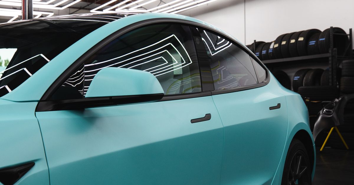 Sleek matte blue car captured inside a modern auto detailing studio with geometric ceiling lights.